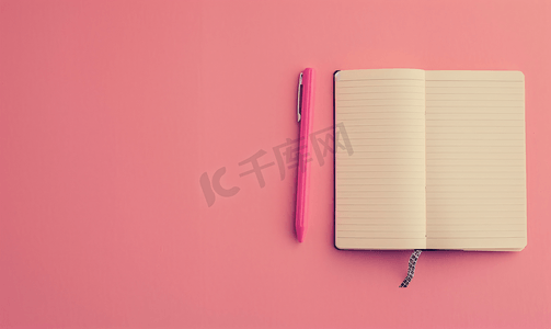 粉红色背景上放着一本打开的笔记本上面有一支笔