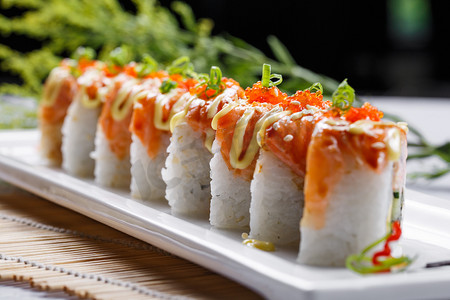 寿司食物摄影照片_长方形瓷盘装的灸三文鱼卷摆放在寿司帘上
