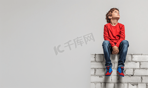孩子思考摄影照片_超级英雄孩子坐在墙上梦想着孤立的白色背景