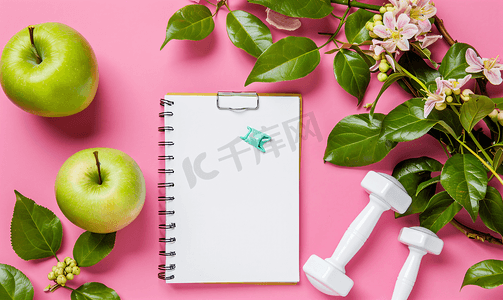 粉红色背景下哑铃苹果和记事本的健身概念