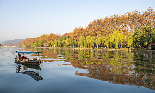 断桥铝窗摄影照片_日出时分杭州西湖湖面上一艘小船划来岸边黄色的树木