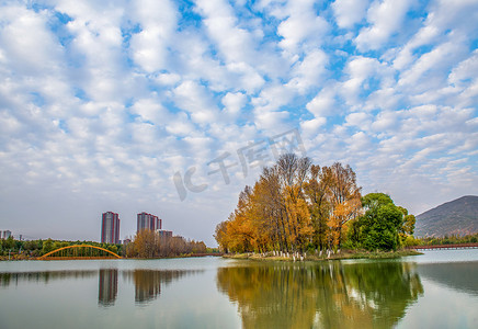 初秋优惠文字排版摄影照片_初秋时节一团团的白云在天空水面上倒影着黄绿相间的树木和高楼