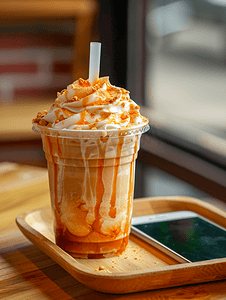 手机模型卡通摄影照片_外卖杯中的泰式奶茶冰沙配有手机旁的木托盘