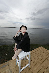 坐姿微调摄影照片_悠闲的坐在美丽湖岸码头的长发少女