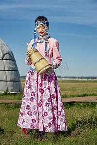 蒙古包前穿蒙古族饰怀抱奶茶桶的蒙族少女