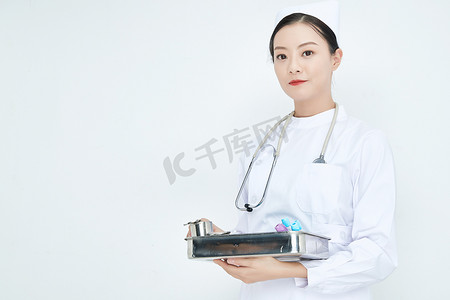 天使圈品管圈摄影照片_身穿护士服手抱化验托盘的年轻女护士