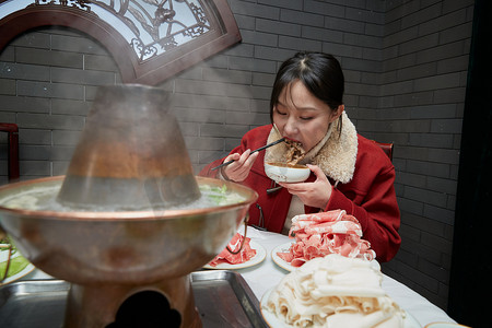 在饭店吃传统铜锅涮肉的亚洲少女