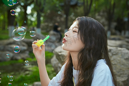 泡泡玩具摄影照片_户外公园里玩吹泡泡的可爱亚洲少女