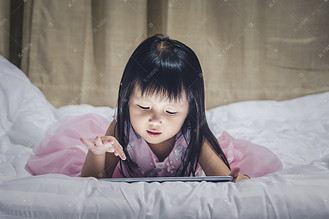 小女孩躺在床上晚上使用互联网观看电视或 gamp 玩儿童智能手机或片剂