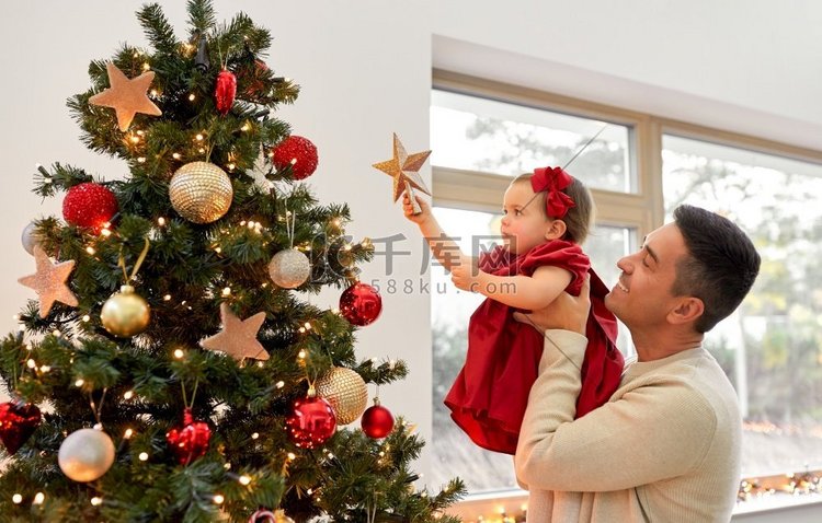 寒假和家庭观念-快乐的中年父亲和小女儿在家里用星星装饰圣诞树。高清摄影大图-千库网