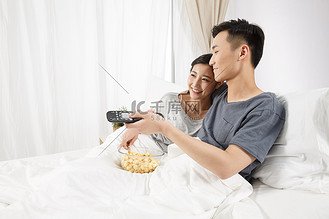 青年情侣坐着床上看电视