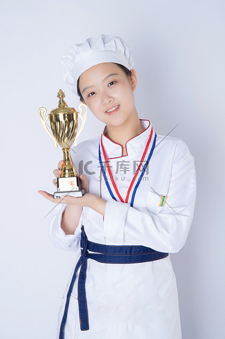 奖杯奖牌证书图片素材_年轻女厨师白天一个女厨师白背景双手拿着奖杯摄影图配图