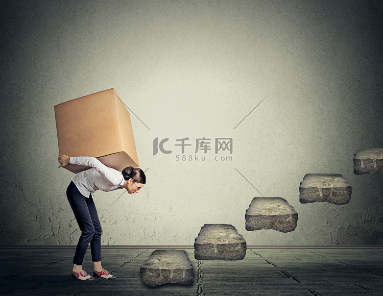 Difficult task concept. Young woman carrying heavy box upstairs高清摄影大图-千库网