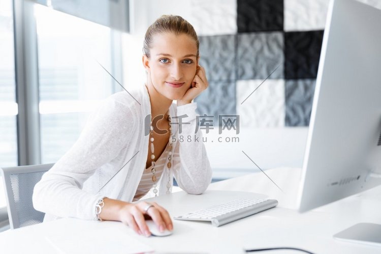 坐在办公桌前的迷人的上班族。坐在办公室办公桌前的漂亮女人高清摄影大图-千库网