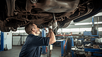 汽车机械师在维修汽车底部零件
