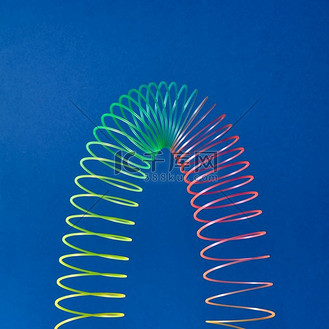在蓝色背景上以抛物线的形式拉伸彩色玩具螺旋,带有复制空间.