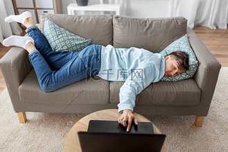 人,无聊和抑郁的概念-无聊或懒惰的年轻人,带着笔记本电脑躺在家里的