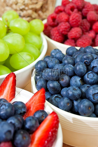 一碗健康的早餐草莓和酸奶蓝莓，背景是树莓、蓝莓葡萄和格兰诺拉麦片或穆埃斯利麦片。