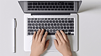 俯视图手打字笔记本电脑在办公桌上工作与笔在笔记本上。
