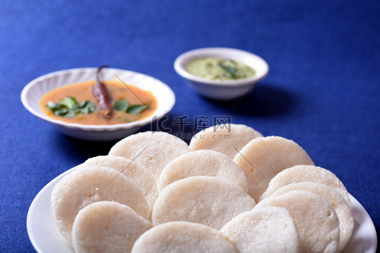 Idli 与 Sambar 和椰子酸辣酱在蓝色背景，印度菜：南印度最喜欢的食物 rava idli 或 semolina idly 或 ...