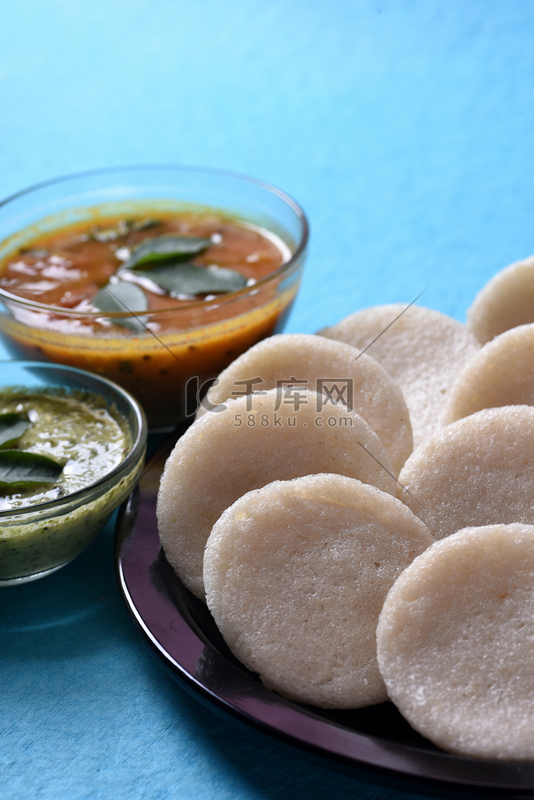 Idli 与 Sambar 和椰子酸辣酱在蓝色背景，印度菜：南印度最喜欢的食物 rava idli 或 semolina idly 或 ...