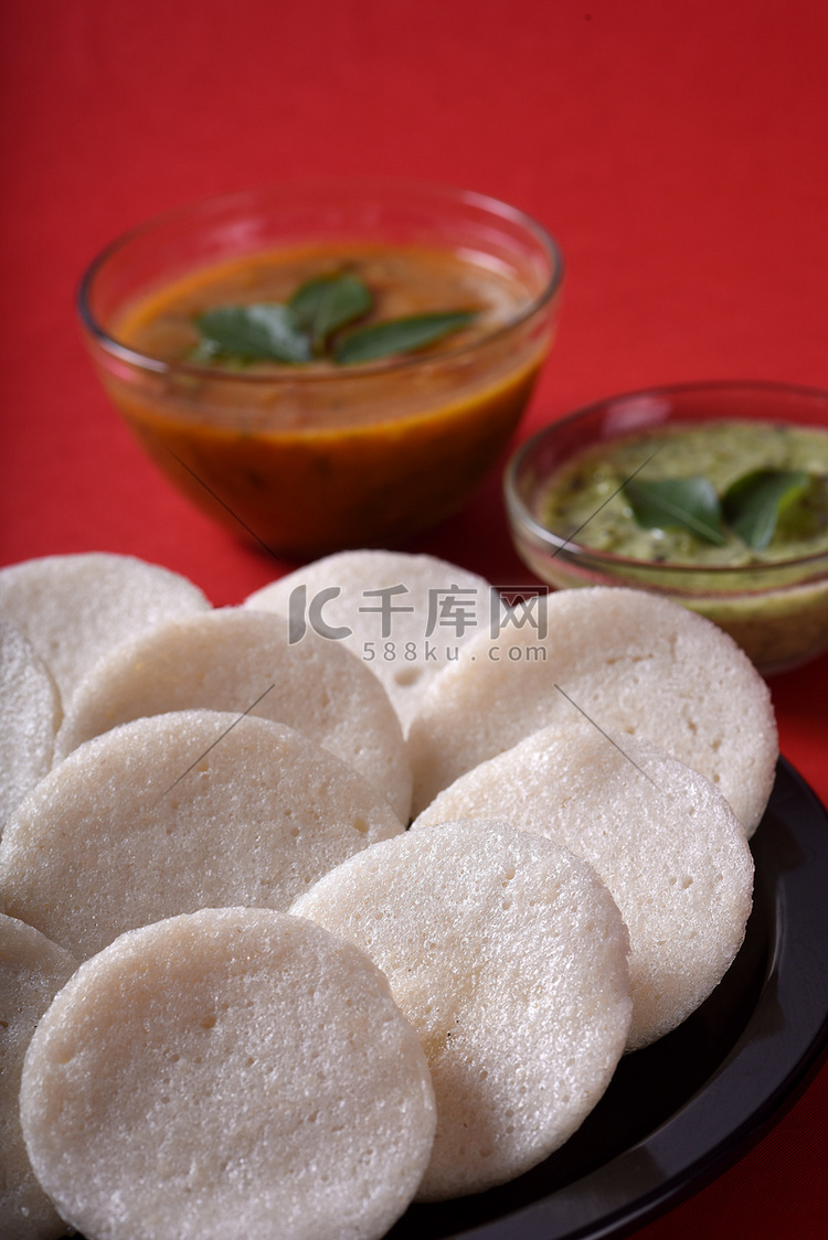 Idli 与 Sambar 和椰子酸辣酱在红色背景上，印度菜：南印度最喜欢的食物 rava idli 或 semolina idly 或 ...