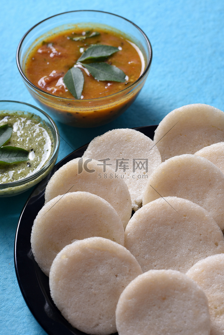 Idli 与 Sambar 和椰子酸辣酱在蓝色背景，印度菜：南印度最喜欢的食物 rava idli 或 semolina idly 或 ...