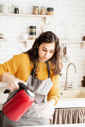 在杯子里的水图片素材_穿着黄色毛衣和灰色围裙的女人准备在厨房里给