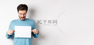 兴奋的留着胡须的男人在空白纸上阅读横幅，展示标志，站在白色背景上