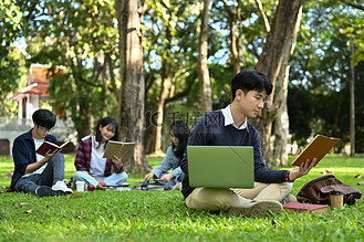 亚洲男学生在大学校园绿色草坪上看书.