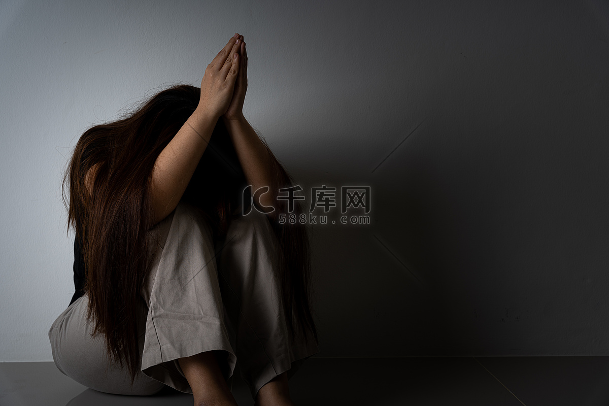 悲伤的女人独自坐在黑暗的房间里抱着膝盖哭泣。高清摄影大图-千库网
