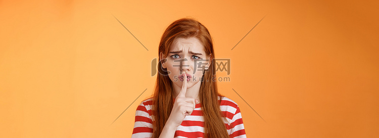 不安、忧虑、没有安全感的红头发女孩乞求保密，皱眉的表情心烦意乱，嘘声，按食指嘴唇嘘声手势，担心有人散布谣言，橙色背景高清摄影大图-千库网