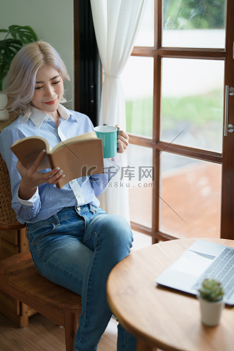 一位亚洲女商人一边喝咖啡一边用桌上的电脑看书的肖像高清摄影大图-千库网