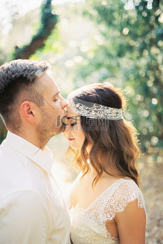新郎在公园里亲吻新娘的额头.