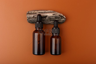 两个透明玻璃瓶，带有皮肤血清或油，用于棕色背景下天然石材上的美甲