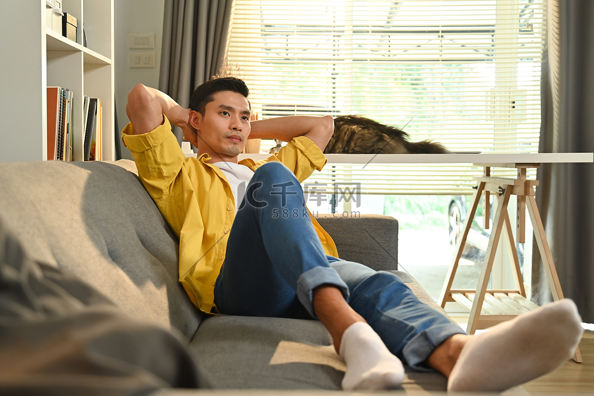 满意的亚洲帅哥双手抱在头后，在家里的沙发上放松高清摄影大图-千库网