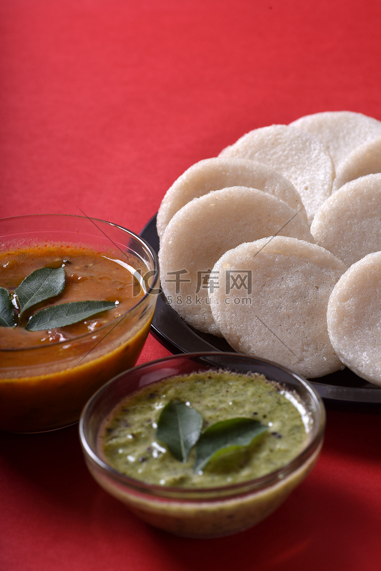 Idli 与 Sambar 和椰子酸辣酱在红色背景上，印度菜：南印度最喜欢的食物 rava idli 或 semolina idly 或 ...