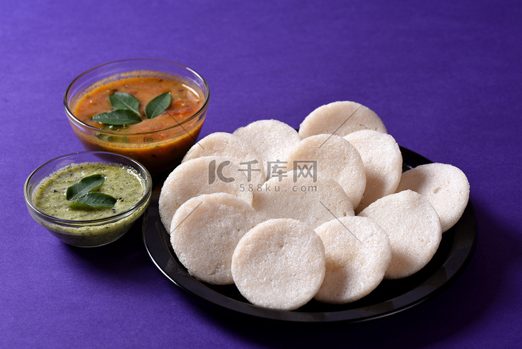 Idli 与 Sambar 和椰子酸辣酱在紫罗兰背景，印度菜：南印度最喜欢的食物 rava idli 或 semolina idly 或 ...