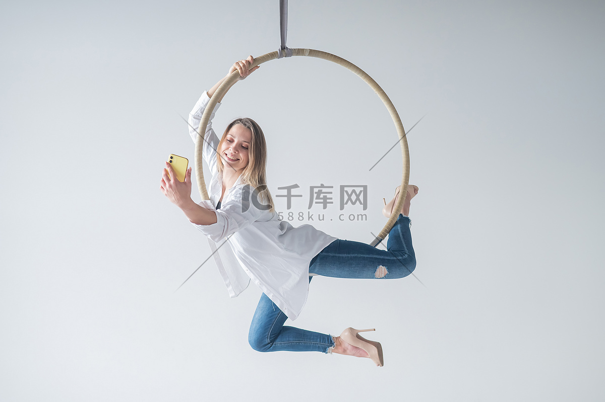 白人女体操运动员做空中吊环练习和使用智能手机。高清摄影大图-千库网