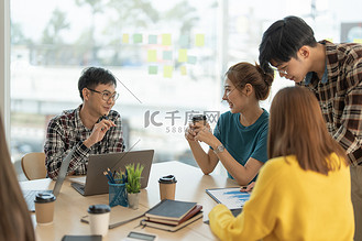 一群亚洲企业在笔记本电脑同事上讨论项目，在共享工作场所结对工作，分析电子文档。