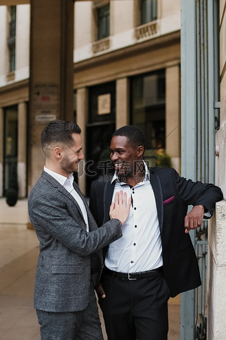 两个快乐的男人,白人和美国黑人,穿着西装在外面的建筑物附近聊天.