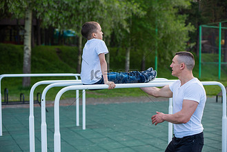 白人男子在操场上的高低杠上训练一个男孩.