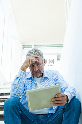 忧心忡忡的成熟男人坐在台阶上拿着平板电脑