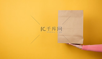 女人手里拿着棕色空白牛皮纸袋，用于黄色背景的外卖。