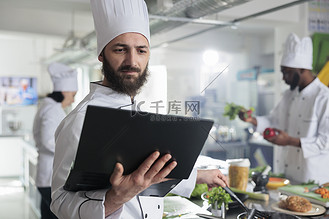 食品工业工人拥有笔记本电脑，按照屏幕上的美食食谱搅拌锅中的配料