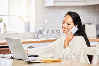 一名混血女性坐在家里的桌子旁，使用笔记本电脑进行远程工作，一边用手机通话，一边在记事本上书写和做笔记。