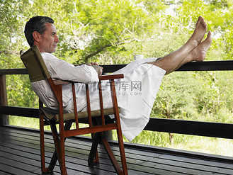 一个穿着浴袍的男人坐在露台椅子上,双脚抬起的全长侧视图