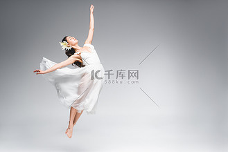 优雅的芭蕾舞女郎在白色礼服跳跃,而灰色背景跳舞