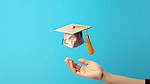 蓝色背景上具有 3D 效果的毕业手抓帽，象征着教育旅程的结束