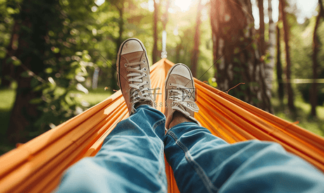 在温暖的夏日露营生活中穿着运动鞋和牛仔裤的男性腿躺在吊床上